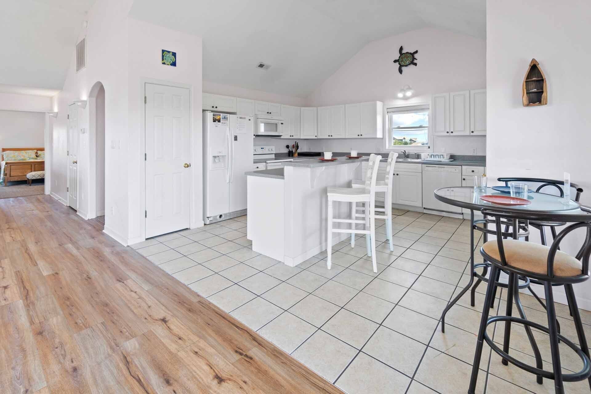 A modern kitchen with white cabinets, a central island, and a dining area with a round table and bar stools.