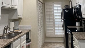 A kitchen with white cabinets, a black refrigerator, and a window with blinds.