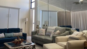 A spacious living room with a high ceiling, large windows, and a modern ceiling fan.