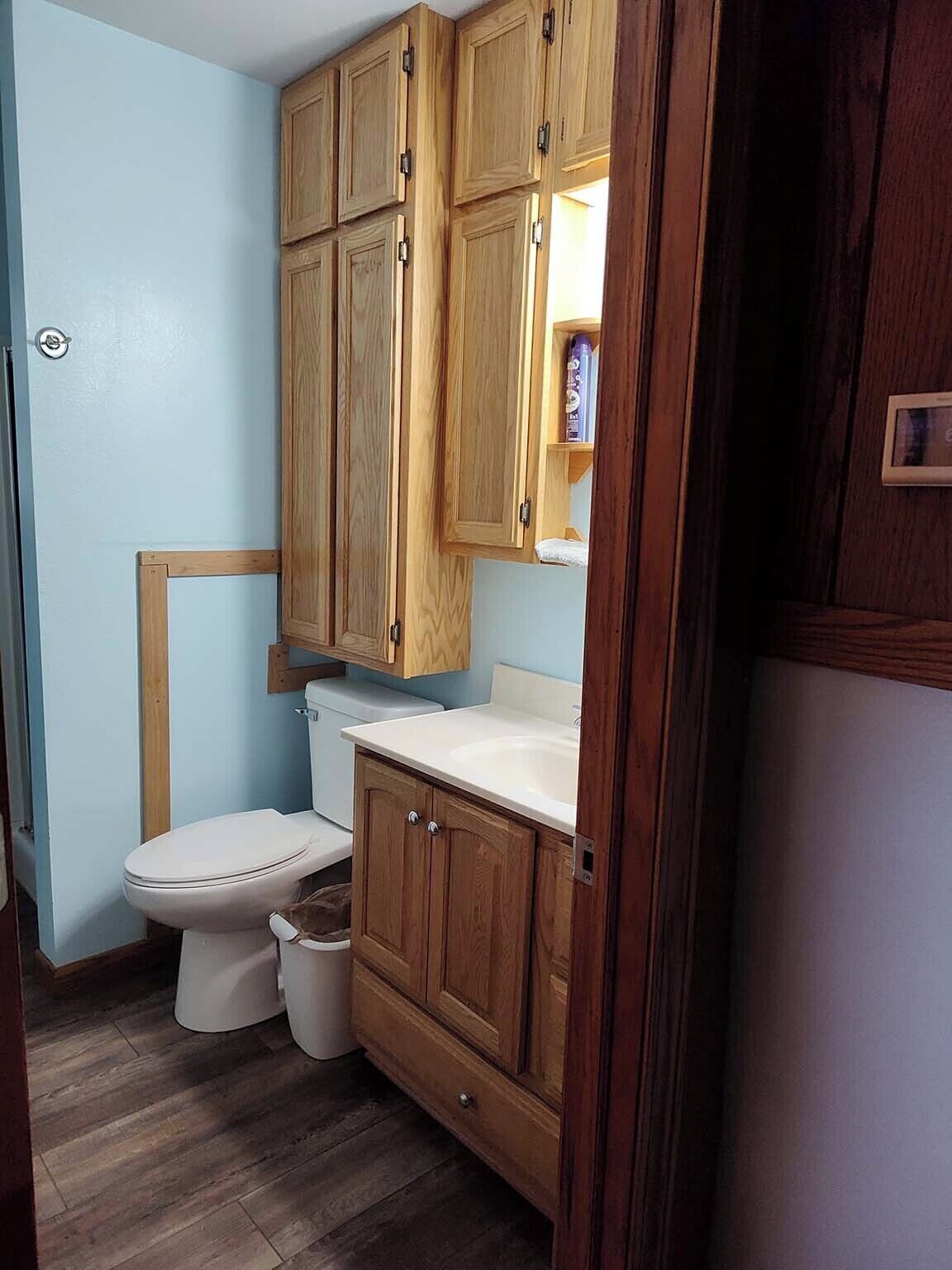 A compact bathroom with a toilet, wooden cabinets, and a white countertop.