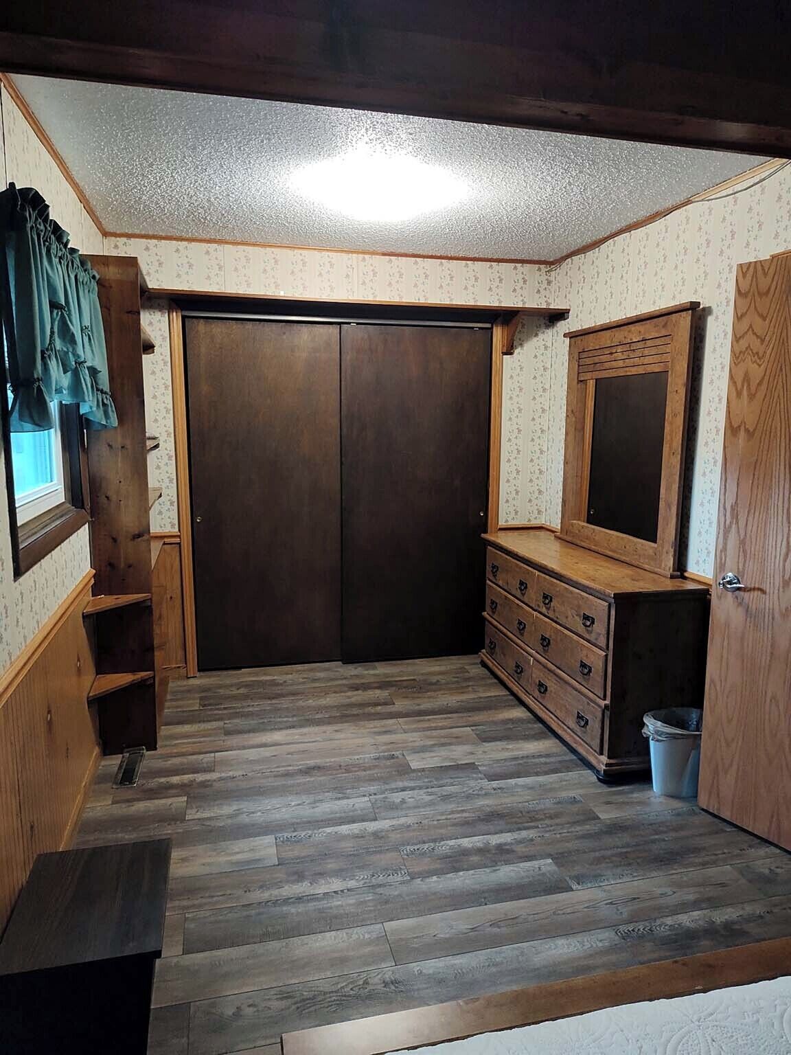 Une pièce avec une armoire en bois, une commode et une fenêtre avec des rideaux.