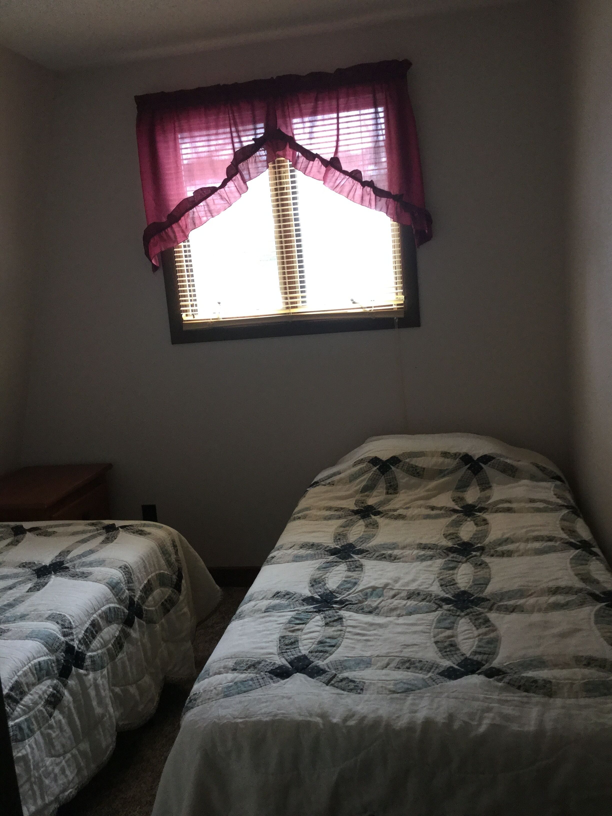 Un dormitorio con dos camas, una ventana con persianas y una mesita de noche de madera.