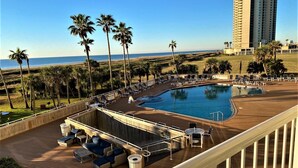 A pool area with lounge chairs and a view of the beach and ocean.