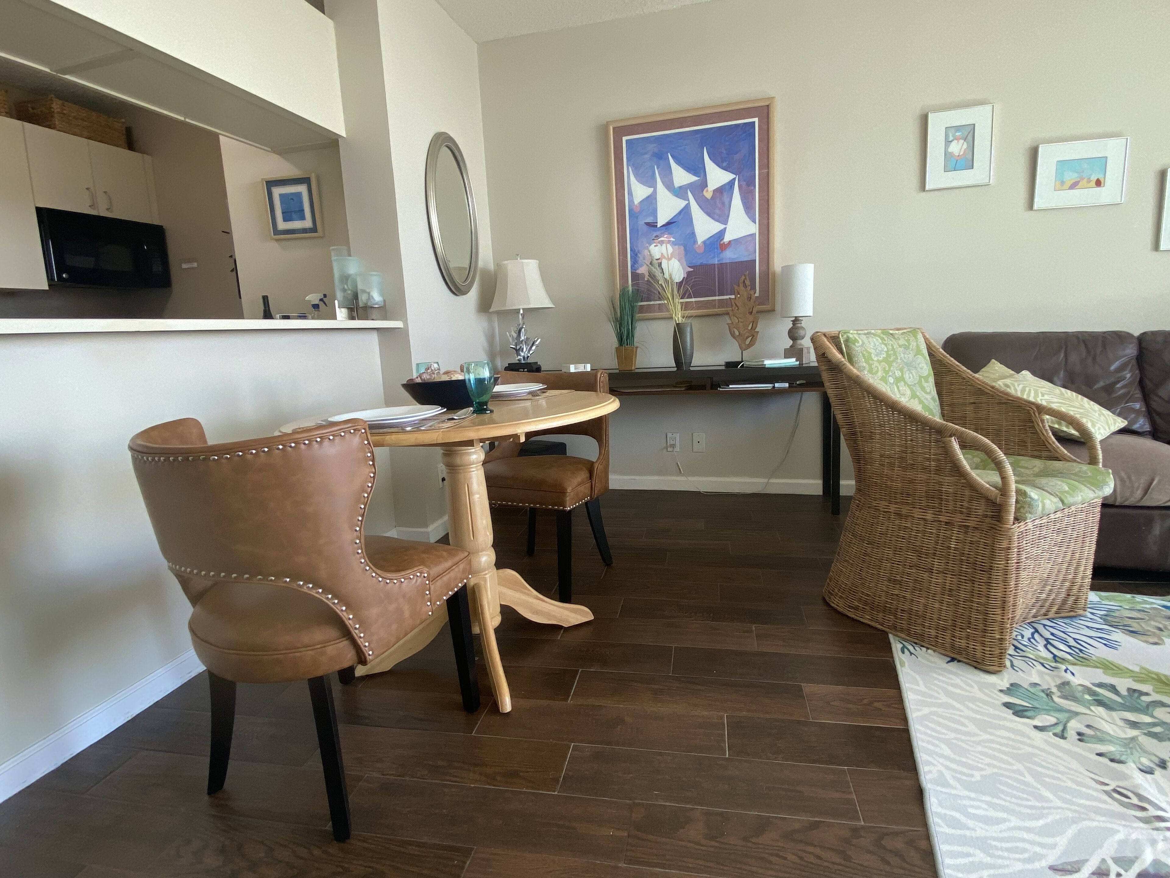 Un comedor con mesa y sillas de madera, una cocina al fondo y una sala de estar con un sofá y un cuadro decorativo.