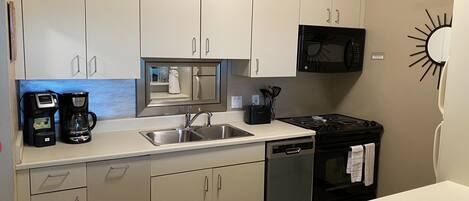 A kitchen with white cabinets, a stainless steel sink, a coffee maker, a microwave, and a stove.