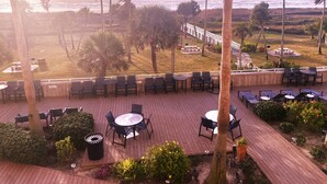 An outdoor patio with tables and chairs, palm trees, and a view of the ocean.