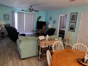 A living room with a sofa, a television, a dining table, and a ceiling fan.