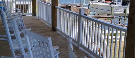A wooden deck with white rocking chairs overlooking a marina with boats and houses.