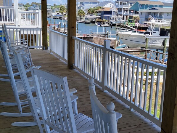 A wooden deck with white rocking chairs overlooking a marina with boats and houses. - Waterfront Beach Cottage on beautiful Holden Beach (Holden Beach)