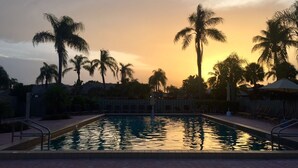 Piscina com palmeiras e pôr do sol ao fundo.