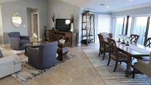 Uma sala de estar ampla com uma televisão grande, assentos confortáveis e uma área de jantar com uma mesa comprida e cadeiras.