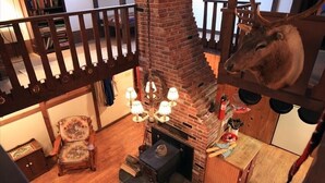 A cozy room with a brick fireplace, a wooden chair, a small table, and a mounted deer head.