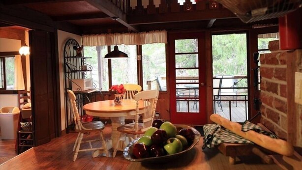 A rustic dining area with a wooden table, chairs, and a bowl of apples.