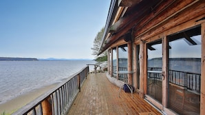 Une terrasse en bois avec une balustrade donnant sur une étendue d’eau, de grandes fenêtres et une vue sur des montagnes lointaines.