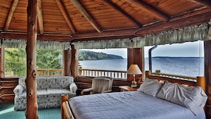 Une cabane avec un intérieur en bois, un lit, un canapé, un fauteuil et une vue sur un lac.