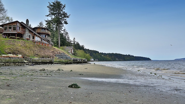 Une propriété située sur la côte, comprenant une maison en bois, un mur de soutènement en pierre et une plage.