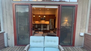A patio with a light blue sofa and two chairs, a sliding glass door leading to a kitchen with wooden cabinets and a refrigerator.
