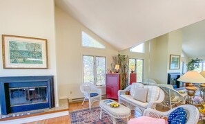 Un salon spacieux avec une cheminée, des meubles en osier et une grande fenêtre.