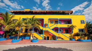 A colorful building with a thatched roof, multiple balconies, and a staircase leading to the upper levels. - One Bedroom Beachfront Efficiency Apartment (Akumal)