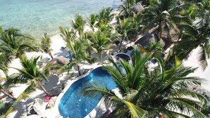 A pool surrounded by palm trees and rocks on a white sandy beach. - One Bedroom Beachfront Efficiency Apartment (Akumal)
