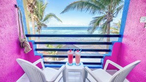 A balcony with two white plastic chairs, a view of the ocean, and a pink wall. - One Bedroom Beachfront Efficiency Apartment (Akumal)