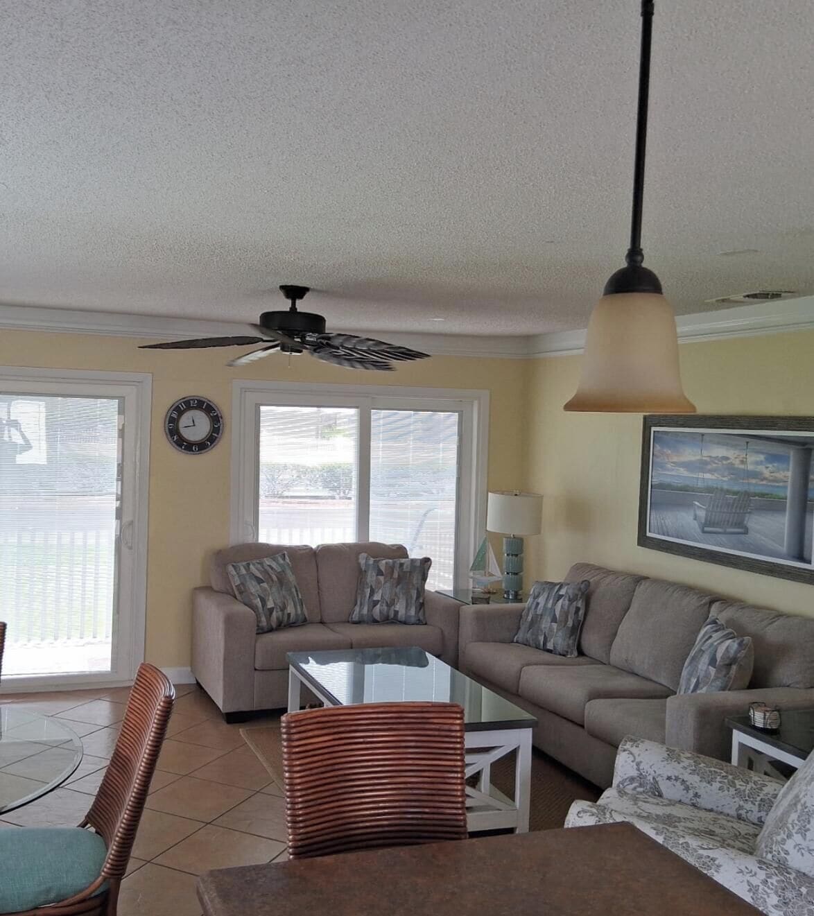 A living room with a ceiling fan, two couches, a glass coffee table, and a chair.