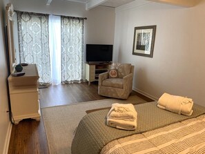 A hotel room with a bed, a chair, a TV, and a desk.