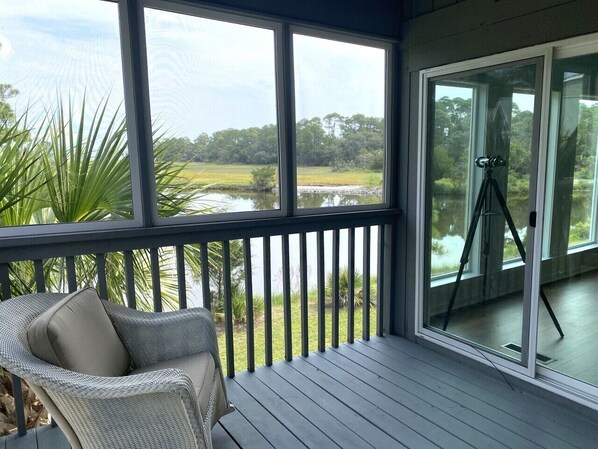 A covered outdoor area with a view of a water body and greenery, a tripod, and a wicker chair.