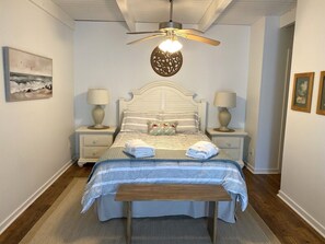 Un dormitorio con una cama, dos mesitas de noche, un ventilador de techo y una lámpara fijada a la pared.