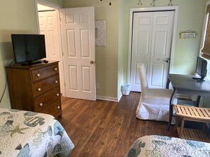 Ein Schlafzimmer mit einem Holzkoffer, einem Fernseher, einem Schreibtisch mit einem Computer und zwei Stühlen.