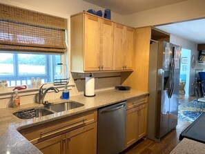 A kitchen with wooden cabinets, a stainless steel refrigerator, a dishwasher, and a window with a view of the outdoors.