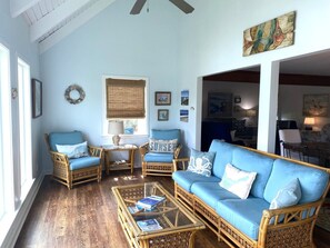 Una habitación con un sofá azul, dos sillones de mimbre, una mesita de centro y una ventana con persianas.