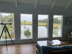 Ein Zimmer mit großen Fenstern und Blick auf ein Gewässer, einem Stativ und einer Sitzecke mit einem Tisch.