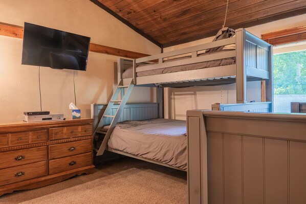 A bunk bed room with a TV mounted on the wall, a wooden dresser, and a window with a view of greenery. - Newly Renovated! - Backyard Forest View on All Three Floors, 30' to Pool/Hot Tub (Breckenridge)