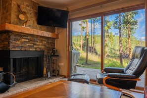 A modern living room with a stone fireplace, a leather chair, and a large sliding glass door leading to a forest view. - Newly Renovated! - Backyard Forest View on All Three Floors, 30' to Pool/Hot Tub (Breckenridge)