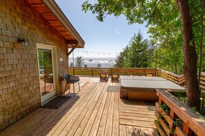 Una terraza de madera con mobiliario exterior, un jacuzzi y vista al océano.