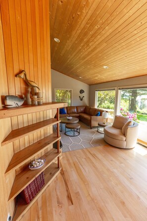 A modern living room with wooden paneling, a sectional sofa, a round coffee table, and a bookshelf with books.