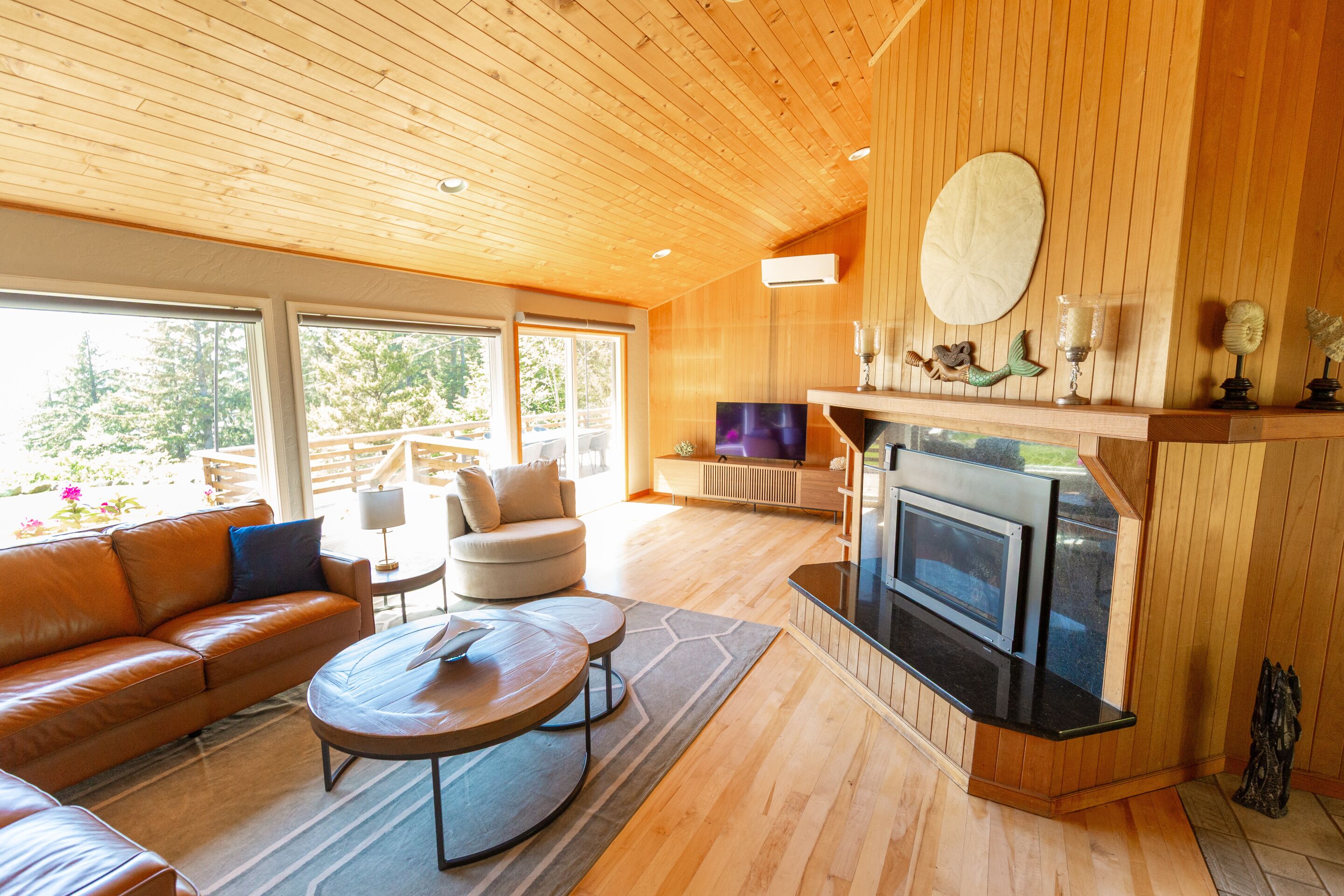 A modern living room with a fireplace, wooden ceiling, and large windows.