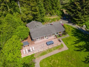 An aerial view of a house with a large deck, surrounded by dense forest.