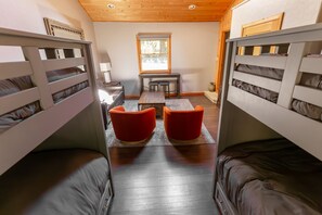 A room with bunk beds, a small table, two red chairs, and a window.