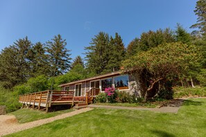 A cabin with a wooden deck, surrounded by lush greenery and trees.