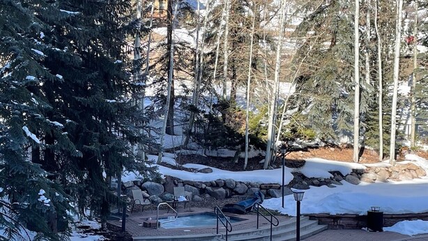 Espacio exterior cubierto de nieve con un jacuzzi, asientos y un muro de piedra.