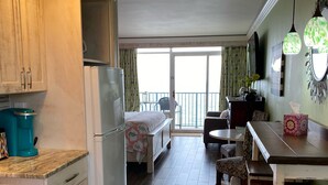 A kitchen with wooden cabinets, a refrigerator, and a coffee maker. There is a dining area with a table and chairs, and a balcony with a view. - A SLICE OF PARADISE! - Direct Oceanfront condo (Myrtle Beach)