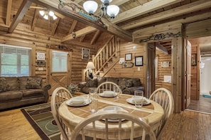 A wooden cabin interior with a dining area, a sofa, and a staircase.