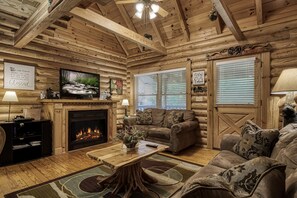 A log cabin interior with a fireplace, wooden walls, a television, and a cozy seating area. - Walking distance to river and outdoor pool access  Free Internet Access sleeps 7 Hot tub and more (Sevierville)