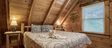 Une chambre confortable dans un chalet en bois, avec un grand lit, deux tables de chevet, une fenêtre avec des stores et un ventilateur de plafond.