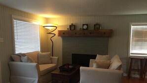 Una sala de estar con dos sofás blancos, una mesa de centro de madera, una chimenea y un reloj de pared.