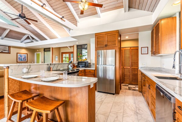 Una cocina amplia con una isla grande, armarios de madera, electrodomésticos de acero inoxidable y un ventilador de techo.