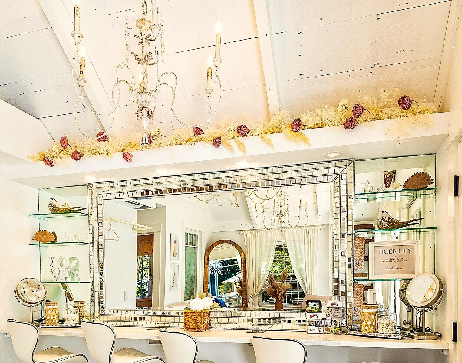 A well-lit vanity area with a large mirror, multiple shelves with decorative items, and a chandelier.