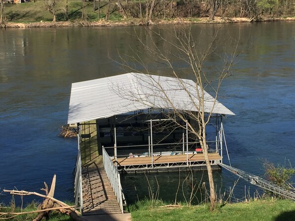 A floating house with a metal roof and a wooden deck, surrounded by calm water.